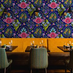 the interior of a restaurant with colorful floral wallpaper and leather booths set up for dinner