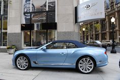 a blue convertible car parked in front of a luxury store on a city side walk