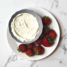 a white plate topped with strawberries next to a bowl of cream