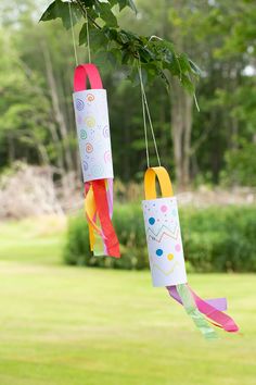 two paper tubes hanging from a tree branch with streamers attached to the ends and colorful ribbons on each end