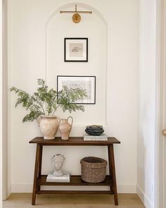 a table with vases and plants on it in front of a white wall that has an arched doorway