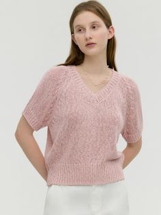 a woman wearing a pink sweater and white pants, with her hands on her hips