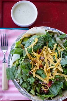 a salad with cheese and dressing in a bowl on a tray next to a fork