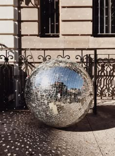 a large mirror ball sitting on top of a sidewalk next to a metal fence and gate