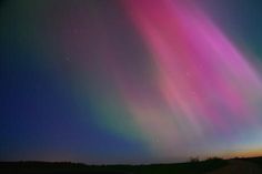 an aurora bore is seen in the night sky over a road and grassy area with trees