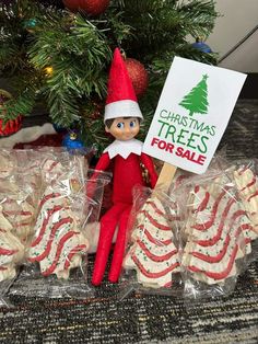 an elf is holding a sign next to some christmas cookies and candies for sale