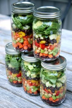 four mason jars filled with salads sitting on top of a wooden table