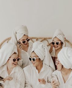 three women in white robes and sunglasses are laying on a bed while reading a book