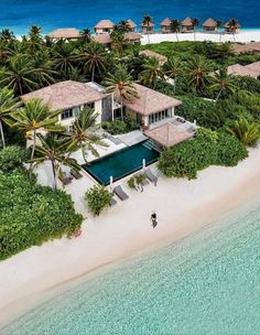 an aerial view of a house on the beach with palm trees and blue water in the background