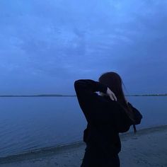 a woman is standing on the beach looking out at the water and holding her hands behind her head