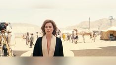 a woman standing in the middle of a desert with people around her and a camera behind her