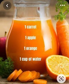 an orange juice in a glass next to carrots and celery