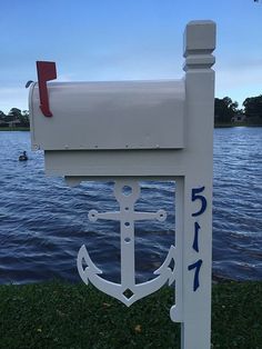 a white mailbox with an anchor on it next to the water in front of a boat