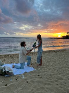 a man and woman sitting on top of a beach next to the ocean at sunset