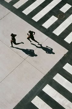 two people running across an airport tarmac with their shadows on the ground and one person walking behind them