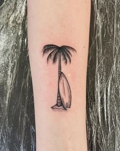 a small palm tree with a surfboard on it's side tattoo by an artist