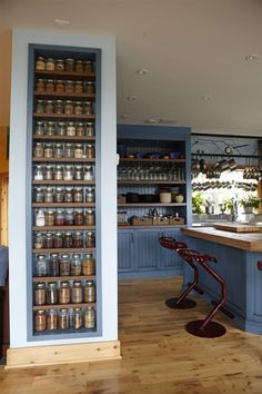 a kitchen with blue cabinets and shelves filled with jars on the wall next to a bar