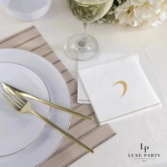 a place setting with white flowers and gold cutlery on the table, next to a glass of wine