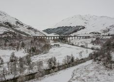 a train traveling over a bridge in the middle of snow covered mountains with trees on both sides