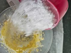 a red and white blender pouring yellow powder into a glass bowl on top of a table