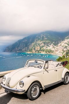 an old white car parked on the side of a road next to water and mountains