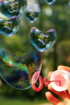 a person is holding soap bubbles in the air with hearts floating out of them,