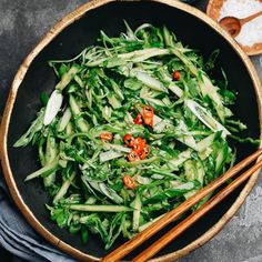 a bowl filled with greens and chopsticks next to some bread on a table