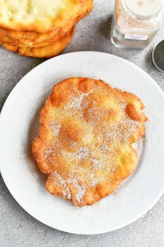 two pastries on a white plate next to a glass of water and salt shakers