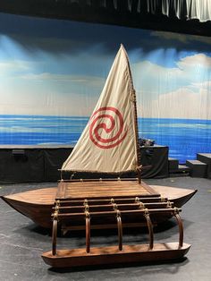 a small wooden boat on display in front of a wall with an ocean scene behind it