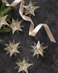 three gold star ornaments next to a white ribbon on a black surface with pine branches