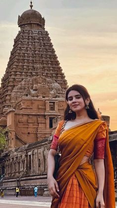 a woman in an orange sari standing next to a tall building with a clock tower