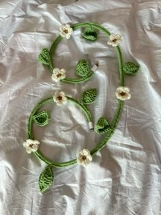 a green crocheted necklace with white flowers and leaves is laying on a sheet