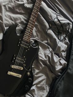 an electric guitar laying on top of a bed next to headphones and a case