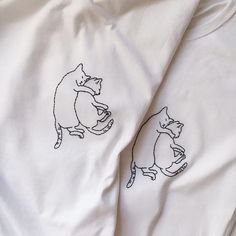 two t - shirts with cats drawn on them sitting next to each other