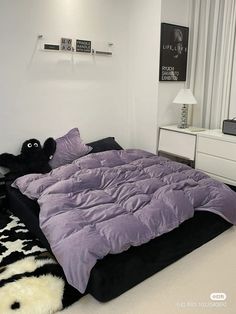 a bed with purple comforter and pillows in a white room next to a window