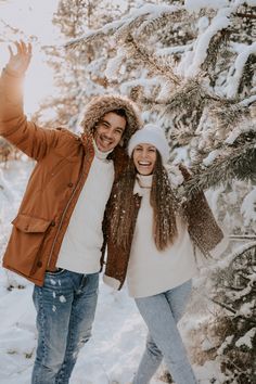 a man and woman standing in front of snow covered trees with their arms up to the camera