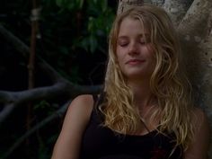 a young woman leaning against a tree in the forest with her eyes closed and looking off into the distance