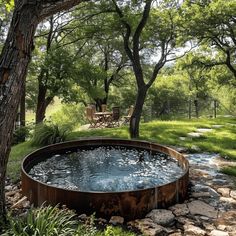 an outdoor hot tub in the middle of a grassy area with trees and rocks around it