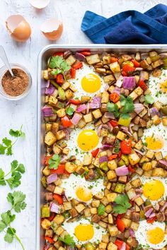 an overhead view of eggs and potatoes in a baking pan with spices on the side