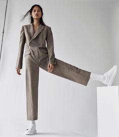 a woman standing on top of a white block wearing a suit and sneakers with her legs spread out