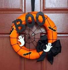 an orange wreath with black ribbon and ghost decorations hanging on the front door for halloween