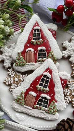 two decorated gingerbread houses sitting on top of a white plate next to pine cones