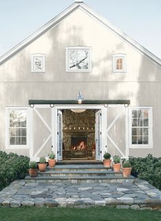 a white barn with potted plants on the front steps and an open fire place