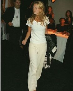 a woman in white is walking down the street with her hand on her hip bag