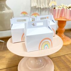 three boxes with rainbow designs on them are sitting on a cake stand in front of a cupcake