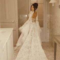 a woman in a white wedding dress standing in a bathroom with her back to the camera