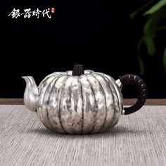 a silver tea pot sitting on top of a wooden table next to a green plant