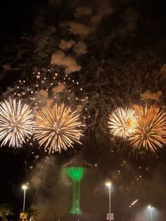 fireworks are lit up in the night sky above a city street and water tower with palm trees