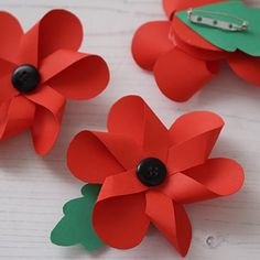 three red paper flowers with green leaves on them