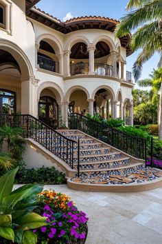 a large house with stairs leading up to the front door and landscaping around it, surrounded by palm trees